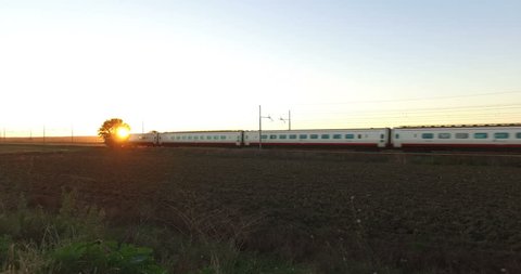 Silhouette of a Passenger Train is Passing in the empty Countryside Land at the Sunset in an Autumnal Day. Travel Concept. 