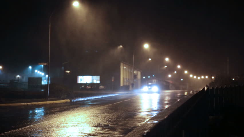 Approaching car headlights under street lights heavy rain storm wind Iceland small town night