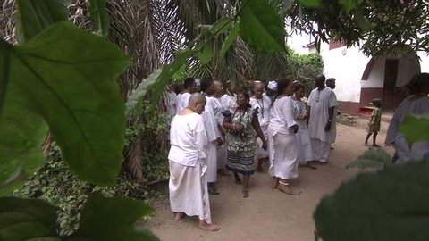 Lagos, Nigeria - August 2013; Women and men dressed in white walk towards Orisha initiation house.