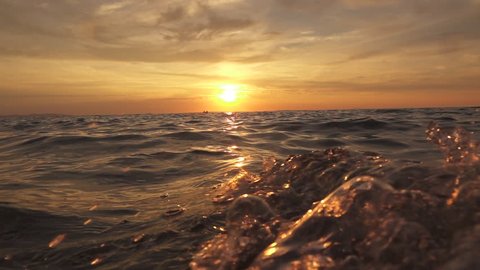 SLOW MOTION, CLOSE UP: Small sailing boat with lovers swinging on rippling sea at magical golden sunset on dreamy tropical island. Big powerful waves swashing to each other and splashing waterdrops