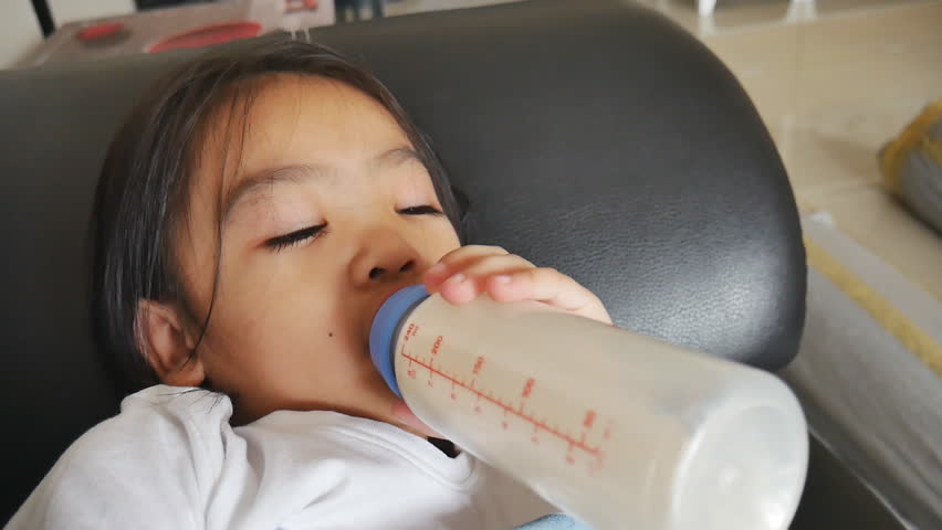 Baby 4 years old happy to drink milk from milk bottle , Asian children drink milk from milk bottle in living room