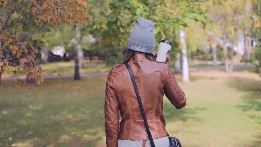 A young woman cheerfully spinning with telephone and coffee in the Park