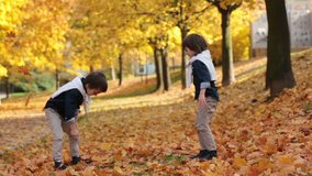 Two fashionable cute kids, throwing leaves in the park, having fun