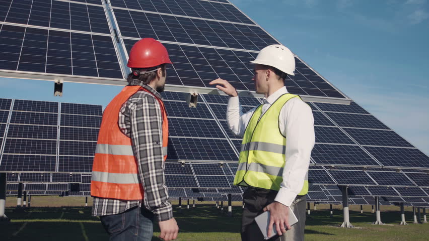 Technicians in long sleeve shirts, reflective vests and hard hats discussing something about solar panel power arrays outside Royalty-Free Stock Footage #20948281