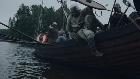 WOLIN, POLAND - 06.08.2016: Viking Warriors Jump off the Row Ship after Arriving to Shore. Slavs and Vikings Festival. Medieval Reenactment. Shot on RED Cinema Camera in 4K (UHD).