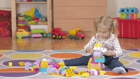 Cute little girl playing with toy blocks at home in room sitting on the floor.