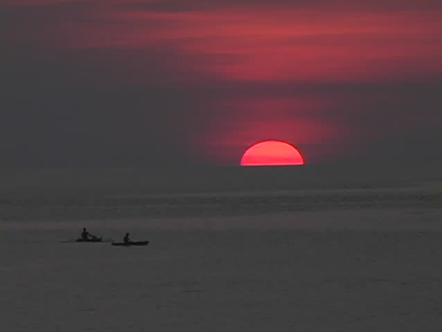 Sun slips below horizon with natives fishing from canoes in the ocean