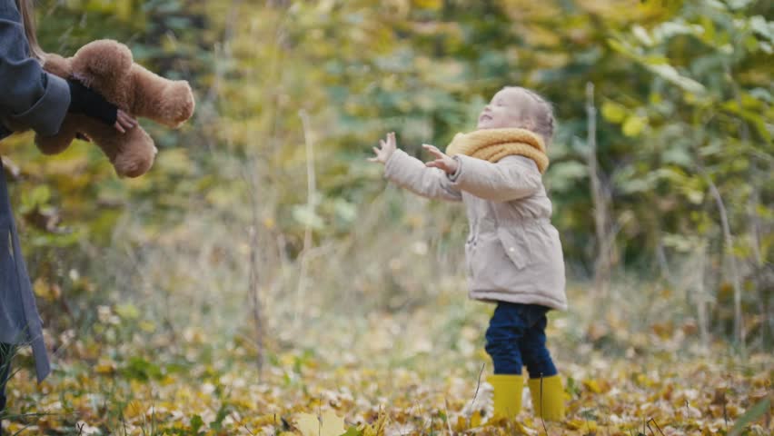 Little blonde girl with her mommy spend time in autumn park - plays with teddy bear
