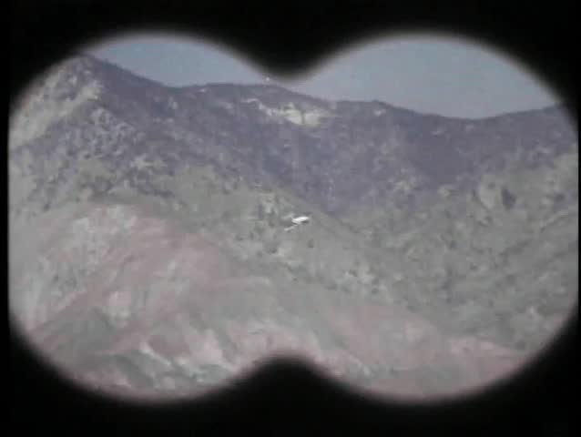 Binocular view of military airplane flying through mountains