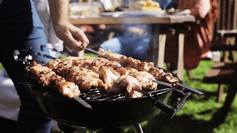 leisure, food, people and holidays concept - man cooking meat on barbecue grill for his friends at summer outdoor party