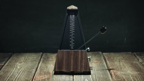 Vintage metronome with golden pendulum beats slow rhythm on the dark background