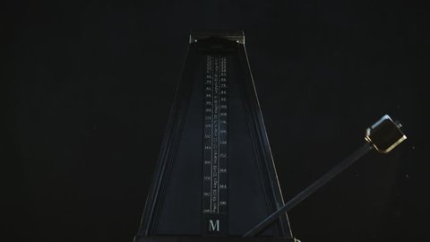 Close-up shot of vintage metronome with golden pendulum beats slow rhythm on the dark background