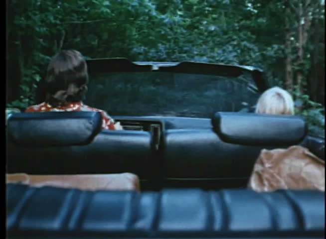 Rear view of man and boy driving through woods in convertible