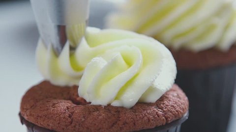 Decorating cup-cake with cream. Using cooking bag, confectioner making multicolor cupcakes for party. Shot of woman's hands putting butter cream on the tasty cakes, home bakery concept