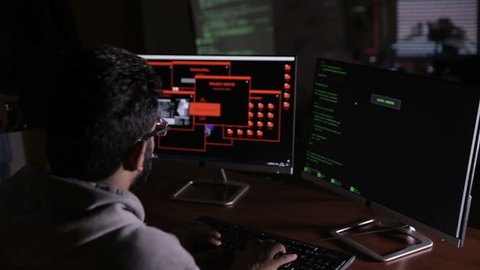 Male arabic hacker hacks computer in dark. Computer code reflecting on his face.