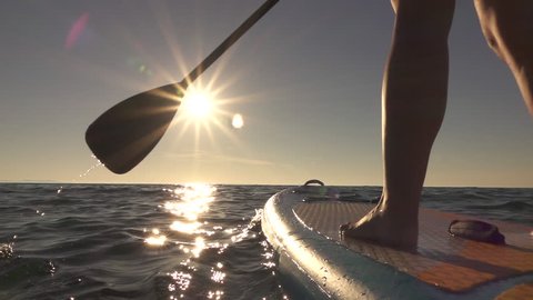 SLOW MOTION, CLOSE UP: Woman standing firmly on inflatable SUP board and paddling. Hands pushing and pulling the paddle through shining water surface and propelling paddleboard on sunny morning