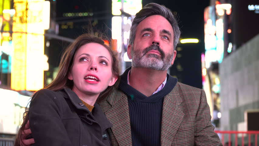 A young attractive romantic couple talk and embrace each other on a date in Times Square, New York City, Manhattan. Speaking and holding arms, rest head on mans shoulder. Display of love and affection