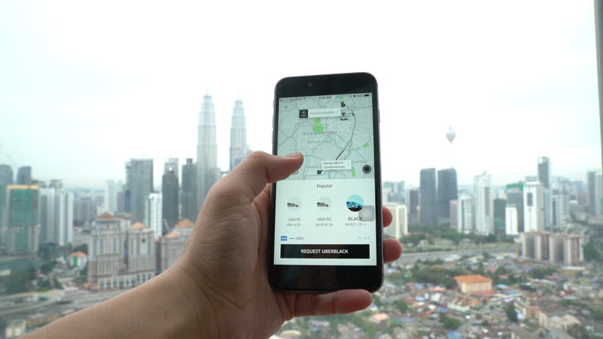 Kuala lumpur, malaysia, circa november 2016 - a uber user looking for a  ride using the uber app on his smartphone, with kuala lumpur city skyline  on the background. 4k video.