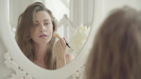 Young woman applies makeup in front of a mirror