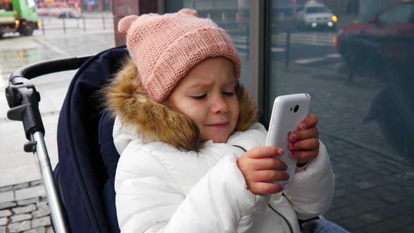 Little child sit in stroller on street play type watch smart phone game cartoon