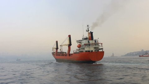 Cargo ship sailing in mist. Tracking shot of the industrial ship. Back view of the red cargo container ship. Istanbul in smog with a cargo ship pass through slowly

