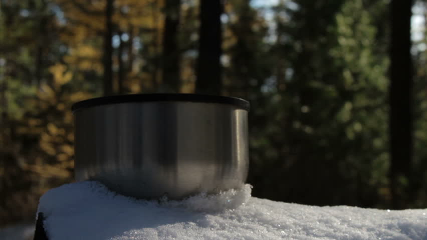 Steaming cup of hot tea or coffee standing on the snow in the forest.