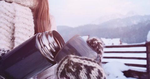 Woman hands in Mittens pouring hot Steaming Tea into a Cup from Thermos, Snowy Mountain View Background. 4K SLOW MOTION 120fps. Close Up. Enjoying Winter Outdoors. Christmas Holidays