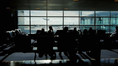 People are waiting for the flight in the airport terminal on a sunny day. Outside the window, the plane takes off. One can see the silhouettes of people, no recognizable faces
