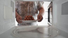 Man cooking sausages in the microwave oven putting plate inside to cook