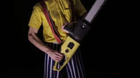 Scary clown with a chainsaw in the dark. Clown murderer threatening you.