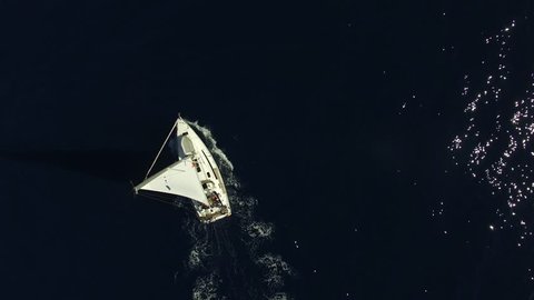 Flying over white yacht in the ocean. Sailing vessel in the sea. The camera is pointing straight down. Aerial view.