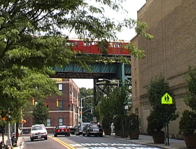 An elevated subway travels over street traffic in Queens, New York City.