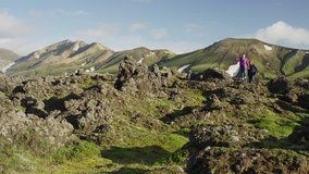 Wide panning shot of of women hiking in green mountain range / Iceland