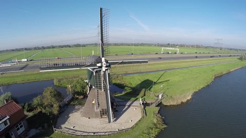 Aerial flying over typical Dutch landscape moving near windmill moving from left to right past canal in polder old Dutch windmill located near water and behind mill modern highway with traffic 4k