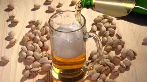 Light beer is poured into a glass on the table with crumbled pistachios. Slow motion 240 fps.  High speed camera shot. Full HD 1080p.