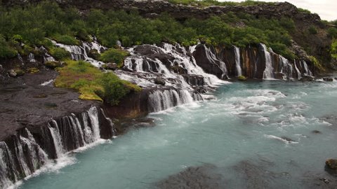 Wide panning shot of waterfalls pouring into river / Hraunfossar, Iceland