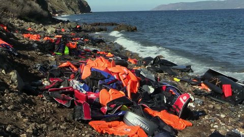 LESVOS, GREECE - NOV 2, 2015: Abandoned by the refugees belongings and life jackets on the rocky shore.