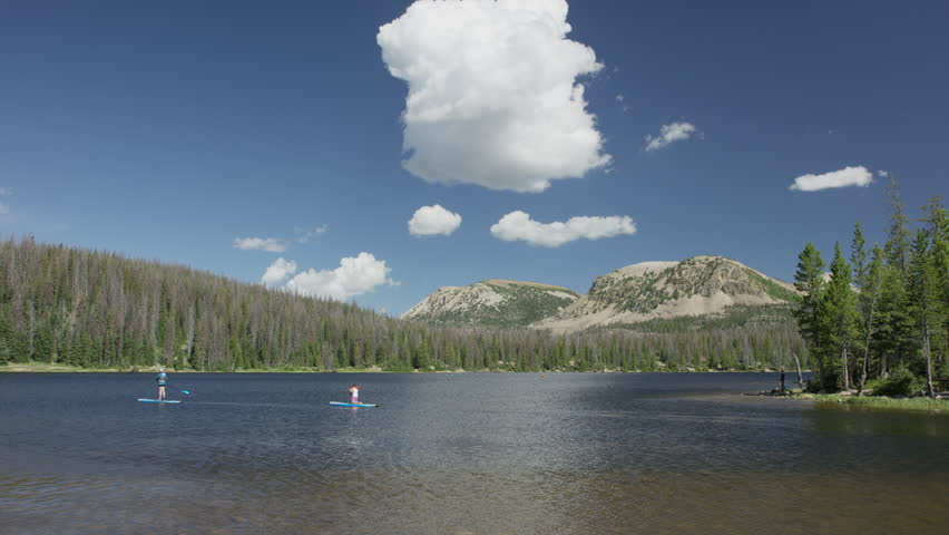 Wide panning shot of paddleboarders on remote mountain lake / Mirror Lake, Utah, United States