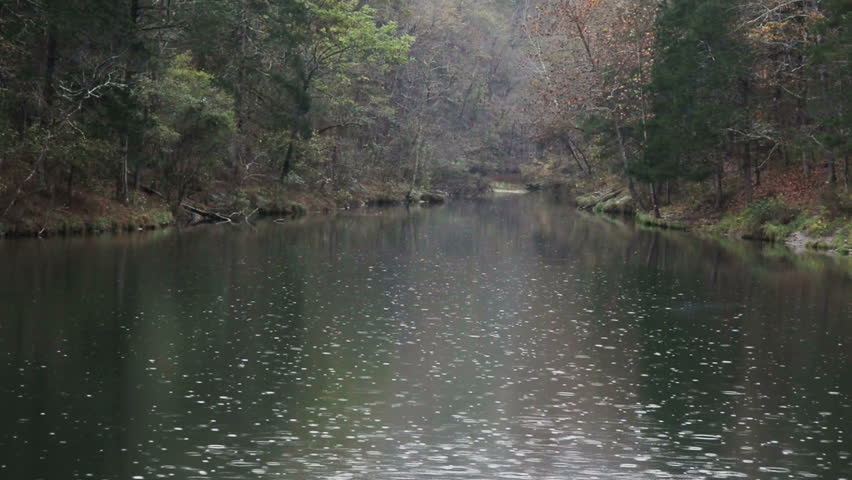 Rain drops fall on the surface of Mirror Lake located in the Ozark Mountains/Ozark National Forest of Arkansas with fish occasionally jumping from the surface. 