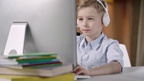 Boy typing on computer keyboard and using headset to speak into microphone