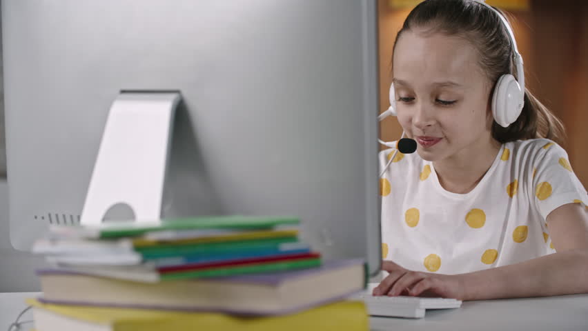 Pretty smiling girl with headset talking and typing something on computer keyboard