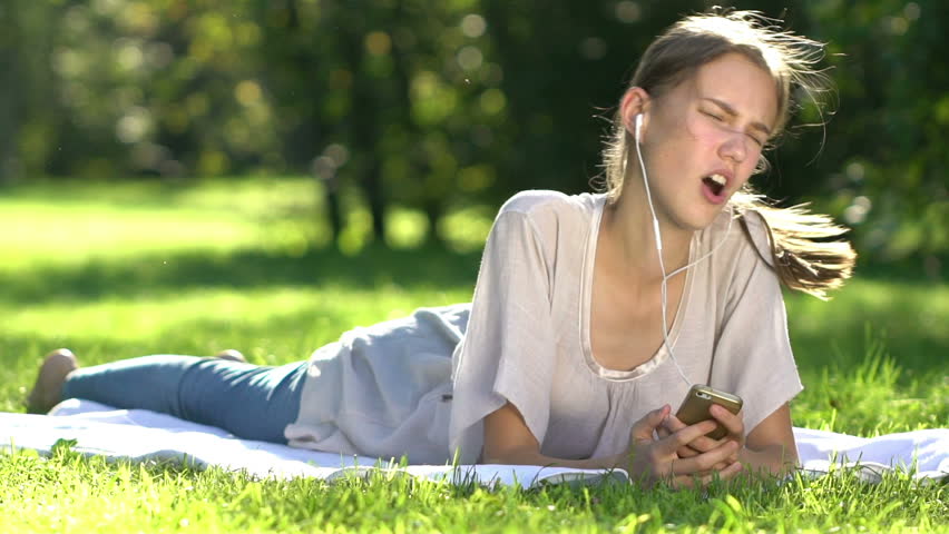 Happy woman Listening to Music and using smartphone in the Park. Slow motion.
