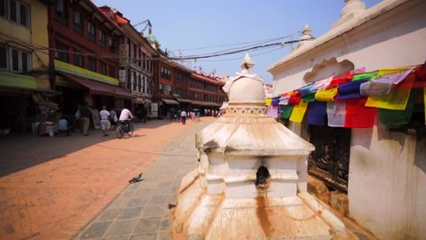 KATHMANDU, NEPAL - APRIL 11, 2016: Walking along colourful prayer flags of the Boudhanath stupa. View of the prayer whheel and white lingam. It's one of most popular tourist sites in Kathmandu area