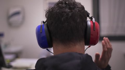 Hearing test. Man with headsets raising his hand when listen to a noise. Occupational health and safety for audiometric testing.