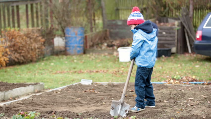 Little boy, shoveling in the garden, digging autumn time
