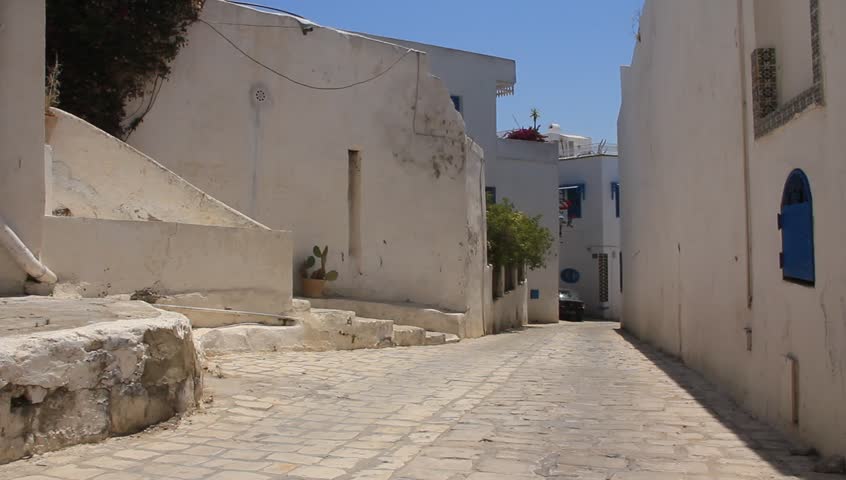 A woman in a colorful dress walks down a side street in Sidi Bou Said, Tunisia