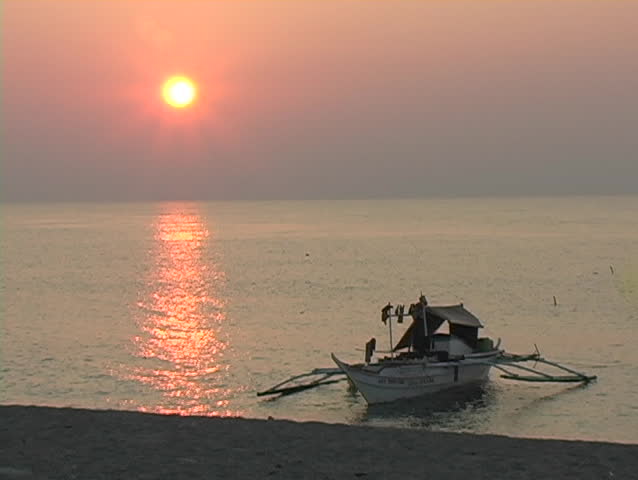 Boat sits in water at beach during sunset