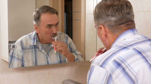 Senior man mustache brush your teeth in the bath. He spits out excess toothpaste in the sink. The concept of purity
