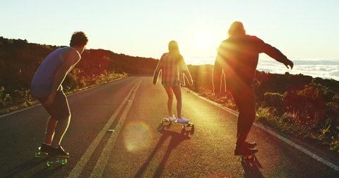 Skateboarders riding down mountain road into the sunset 