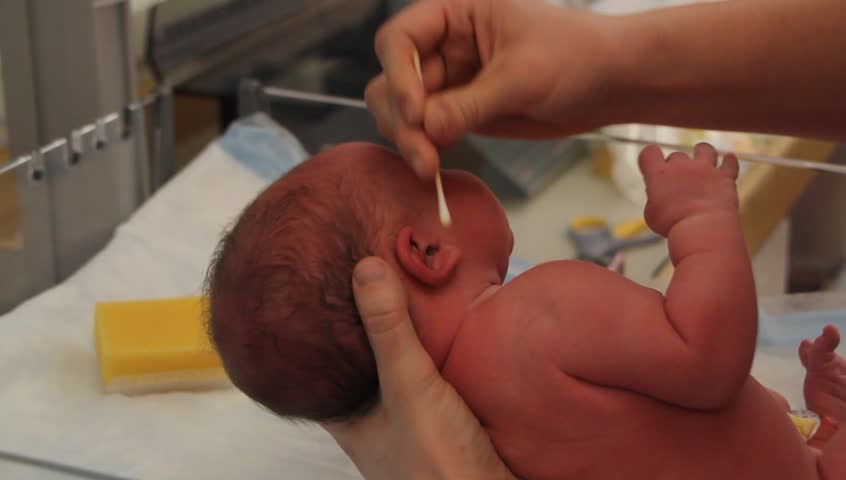 A newborn baby at the hospital getting his ears cleaned by the nursing staff 